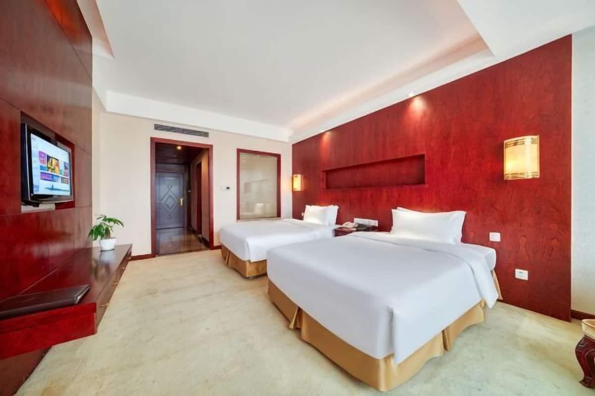 Une chambre d’hôtel avec deux lits, une télévision, un bureau et un mur d’accent de couleur rouge.