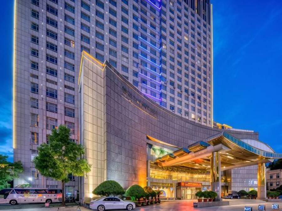 A high-rise hotel with a modern entrance and a large parking area.