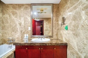 A bathroom with a marble wall, a sink with a mirror, a towel rack, and a bathtub.