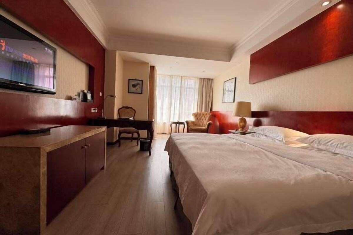 Une chambre d’hôtel équipée d’un lit, d’un bureau, d’une chaise, d’une télévision et d’une fenêtre avec des rideaux.