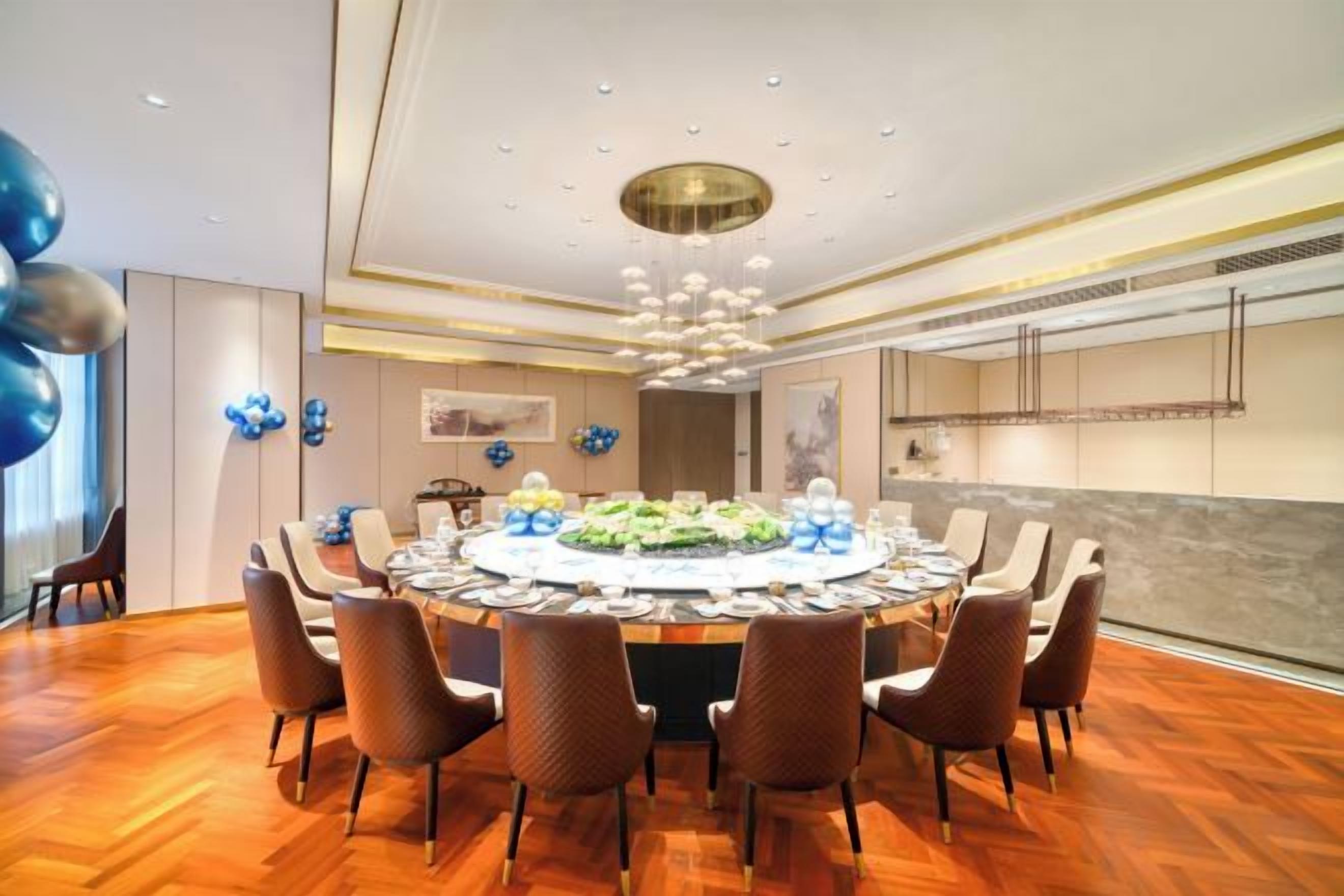 A round dining table with chairs, a chandelier, and a view of a kitchen in the background.