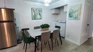 A modern kitchen with a stainless steel refrigerator, a dining table with chairs, and a potted plant. There are two wall-mounted washing machines and a ceiling light fixture. - Duplex - Unit B Near DWTN & Austin-Bergstrom Airport (Austin)