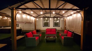 A covered outdoor seating area with wicker furniture and red cushions, under a roof with string lights. - Duplex - Unit B Near DWTN & Austin-Bergstrom Airport (Austin)