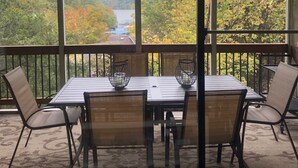 Een overdekte eethoek met een tafel en stoelen, met uitzicht op een rivier en herfstkleuren.