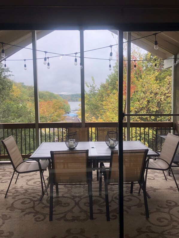 A covered outdoor dining area with a table and chairs, overlooking a scenic view of a river and autumn foliage.