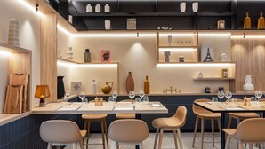A modern restaurant interior with multiple dining tables and chairs, warm lighting, and various decorative items on shelves. - Courtyard by Marriott Paris Charles de Gaulle Central Airport (Roissy-en-France)