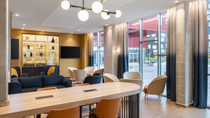 A modern hotel lobby with a wooden reception desk, comfortable seating, a decorative display case, and large windows offering a view of the outside. - Courtyard by Marriott Paris Charles de Gaulle Central Airport (Roissy-en-France)