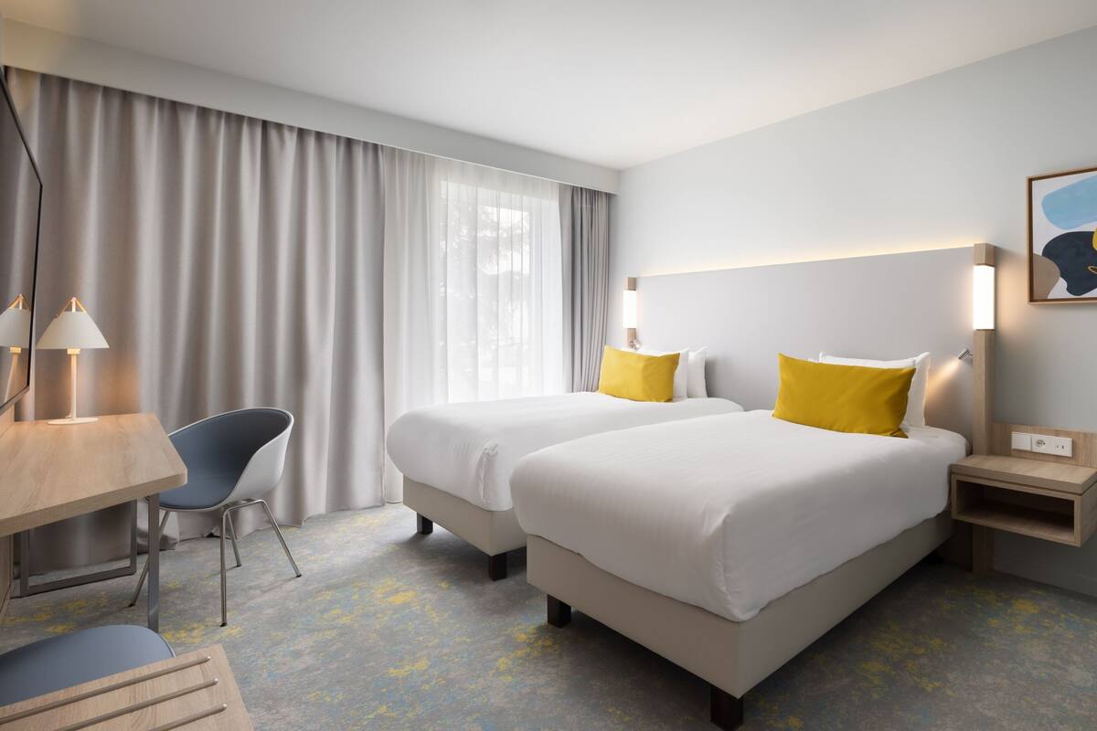 Una habitación de hotel con dos camas, un escritorio, una silla y una mesita de noche.
