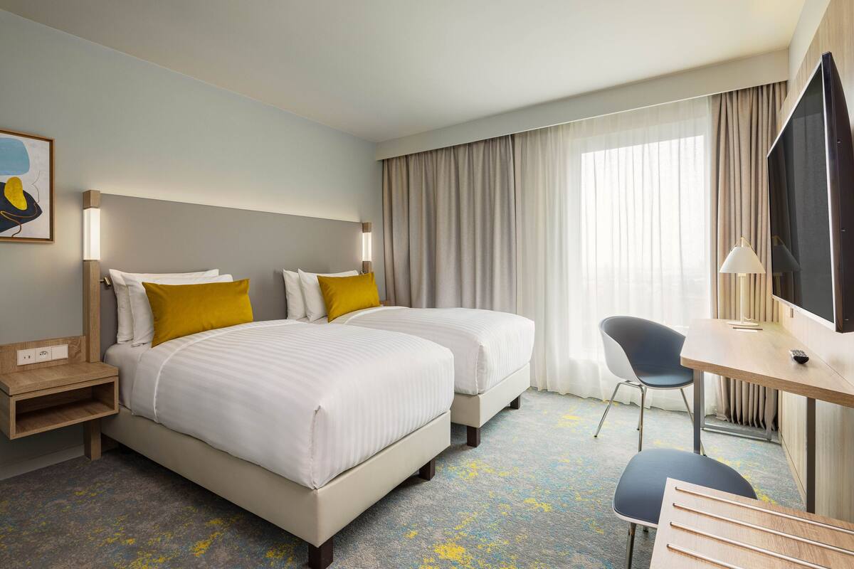 Habitación de hotel con dos camas, un escritorio, una silla y un televisor.