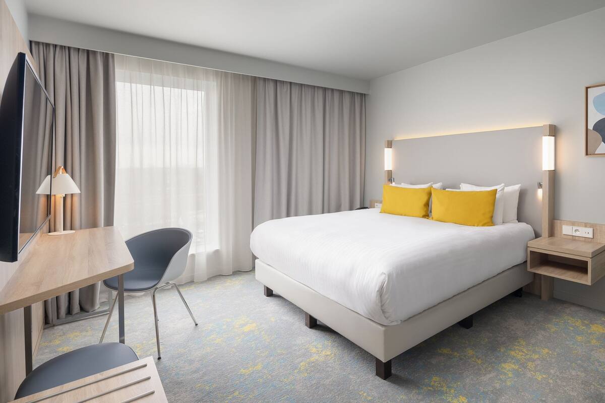 Una habitación de hotel con una cama, un escritorio, una silla, un televisor y una mesita de noche.