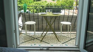 En balkon med flisegulv, to hvide stole, et lille rundt bord og en grøn parasol.