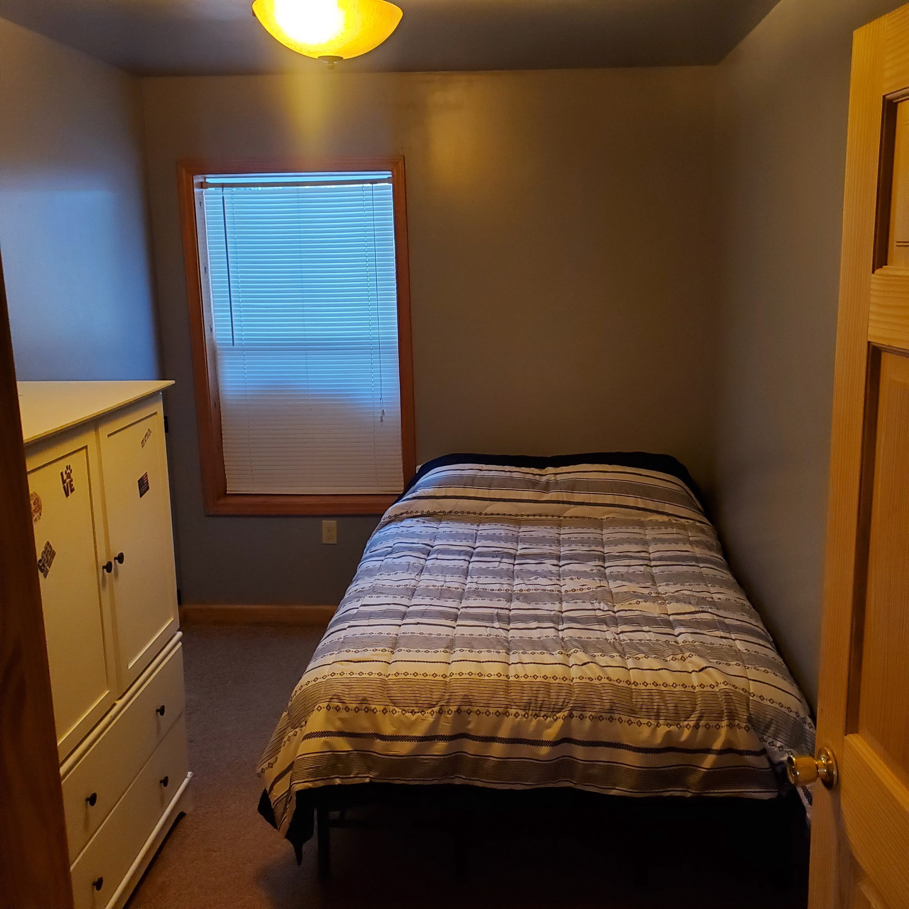 A small bedroom with a single bed, a dresser, and a window with blinds.