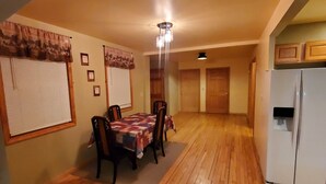 A dining area with a wooden table and chairs, a refrigerator, and a ceiling light.
