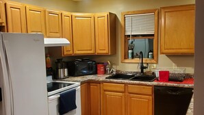 A kitchen with wooden cabinets, a white refrigerator, a stove, a sink, and a window with blinds.