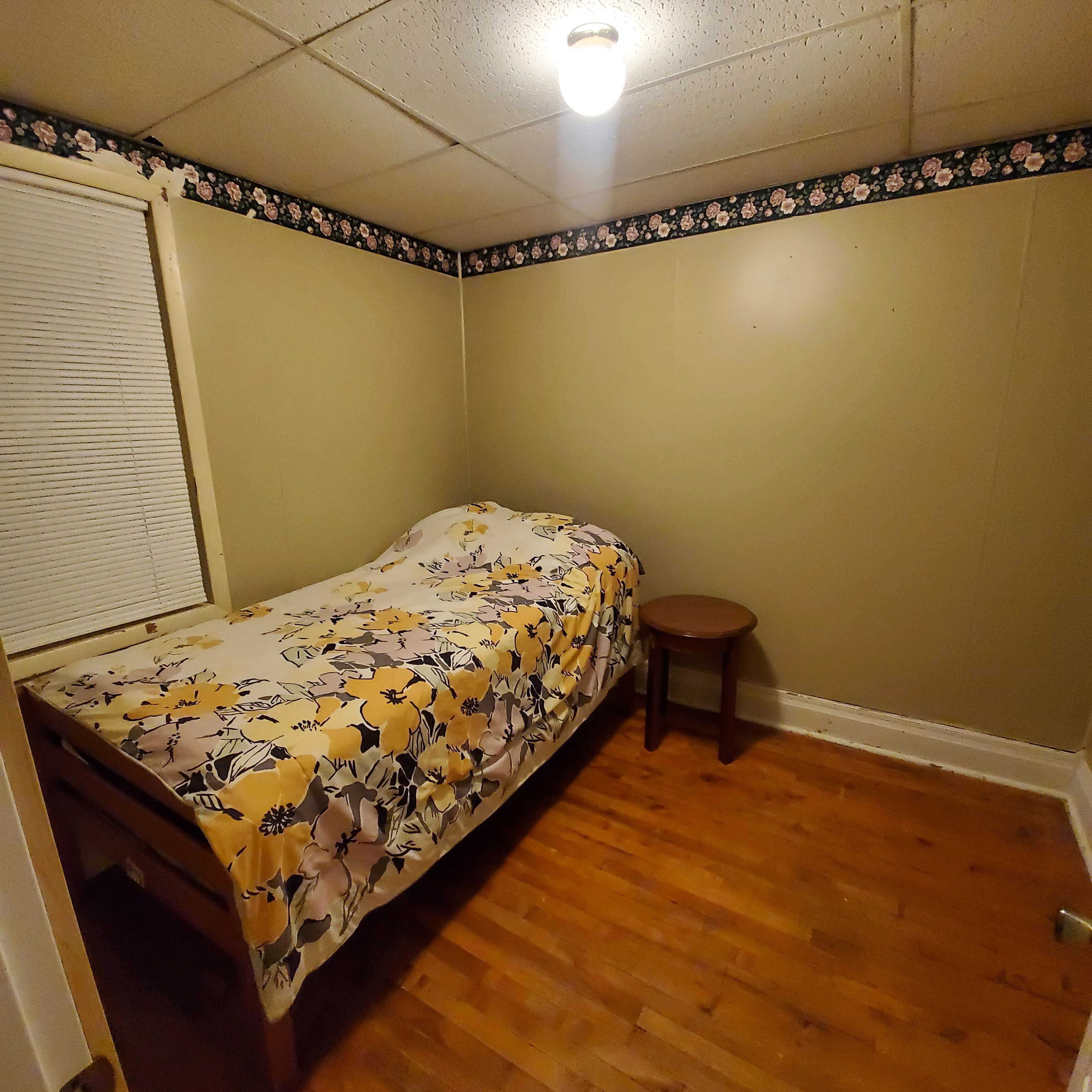 Un dormitorio pequeño con una cama individual, piso de madera y un taburete.