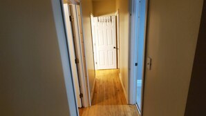 A narrow hallway with wooden flooring and white doors on both sides.