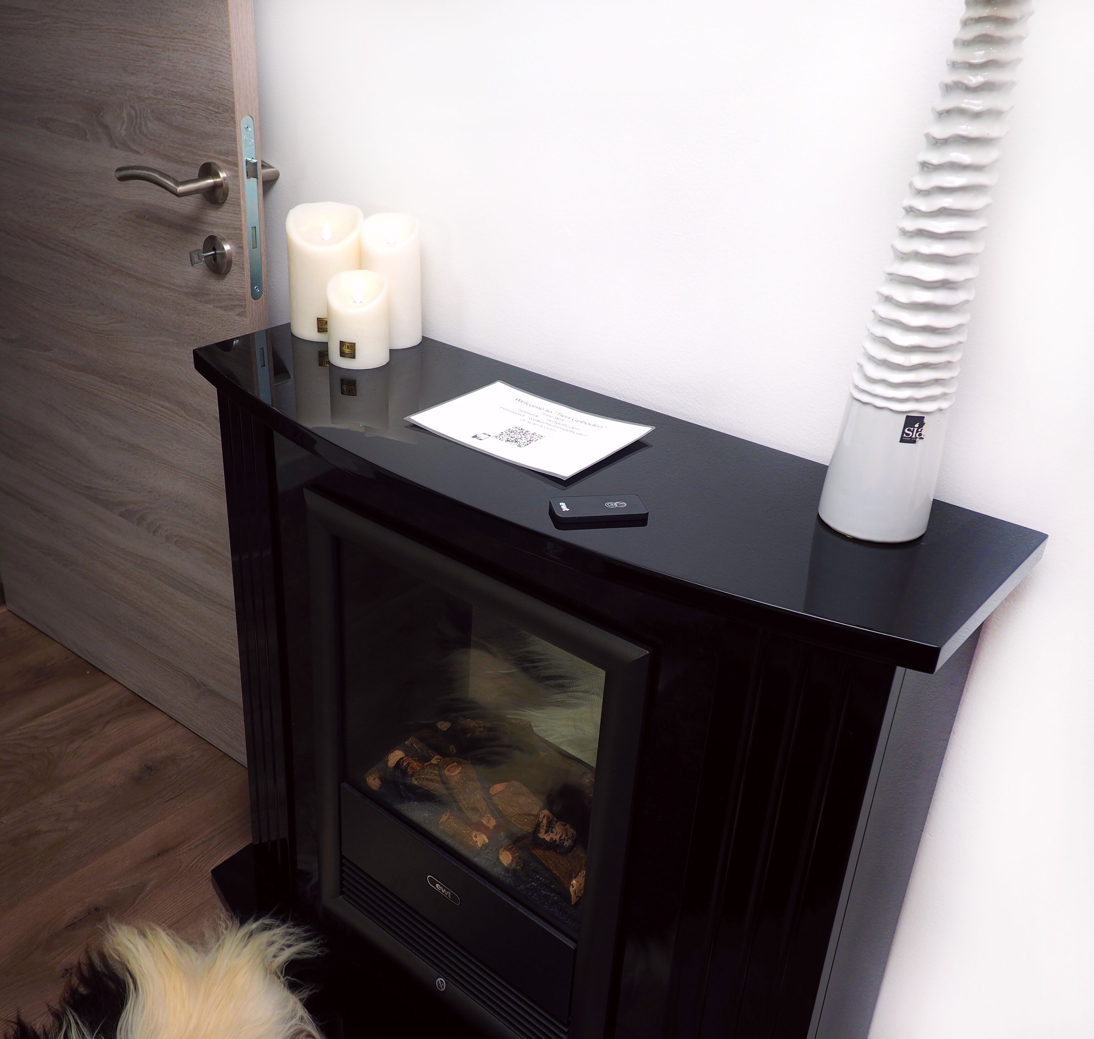 A modern fireplace with three lit candles, a QR code, and a small black object on the mantel.