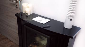 A modern fireplace with three lit candles, a QR code, and a small black object on the mantel.