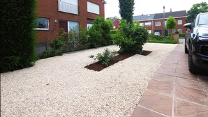 A residential area with a gravel driveway, a black car parked on the street, and a brick building with two garage doors. - Comfortable apartment, close to downtown and train station (Brugge)