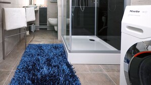A modern bathroom with a glass-enclosed shower, a toilet, and a washing machine. - Comfortable apartment, close to downtown and train station (Brugge)