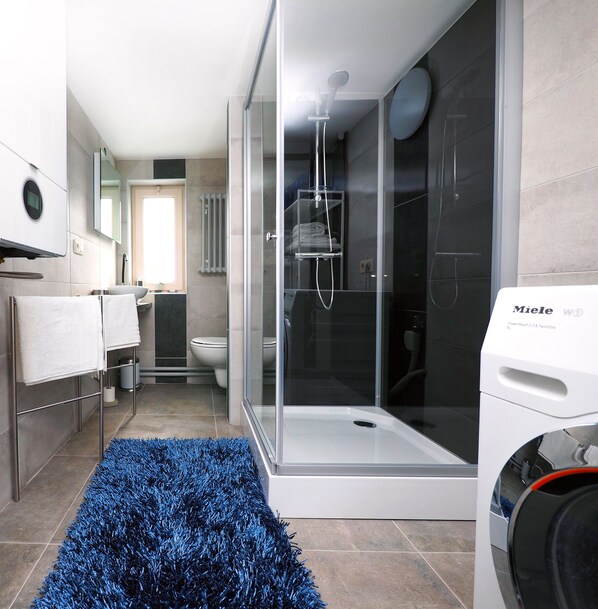 A modern bathroom with a glass-enclosed shower, a toilet, and a washing machine. - Comfortable apartment, close to downtown and train station (Brugge)