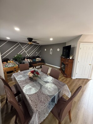 A dining area with a table set for four, a sofa, a fireplace, and a ceiling fan.