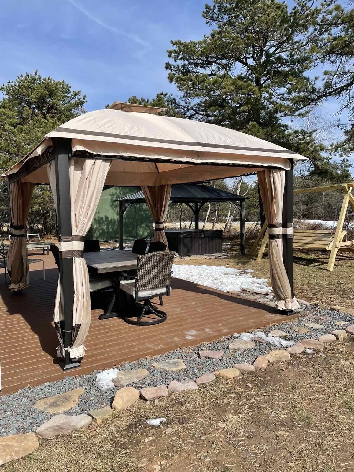 A covered outdoor dining area with a table and chairs, surrounded by a wooden deck and a stone border.