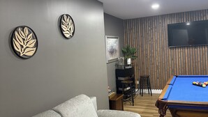 Een moderne woonkamer met een grijze bank, een pooltafel, een flatscreen-tv en een houten accentmuur.