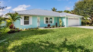 A single-story house with a garage, surrounded by a well-maintained lawn and tropical plants. - New Construction- Hot Tub - 1.3m to Beach, 2 KING Beds. (Hobe Sound)