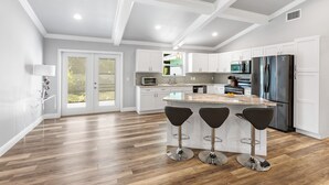 A modern kitchen with white cabinets, a stainless steel refrigerator, and a central island with bar stools. - New Construction- Hot Tub - 1.3m to Beach, 2 KING Beds. (Hobe Sound)