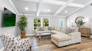 A living room with a sectional sofa, a star-patterned armchair, a coffee table, a large potted plant, and a painting of a forest. - New Construction- Hot Tub - 1.3m to Beach, 2 KING Beds. (Hobe Sound)