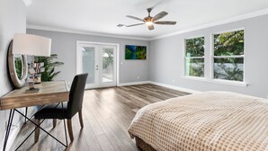 A bedroom with a bed, a desk with a chair, a ceiling fan, and large windows. - New Construction- Hot Tub - 1.3m to Beach, 2 KING Beds. (Hobe Sound)