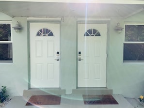 A house with two white doors, each with a small window above. There are two light fixtures on either side of the doors.
