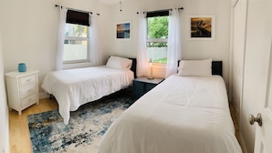 A bedroom with two single beds, a nightstand, a lamp, and a window with curtains.