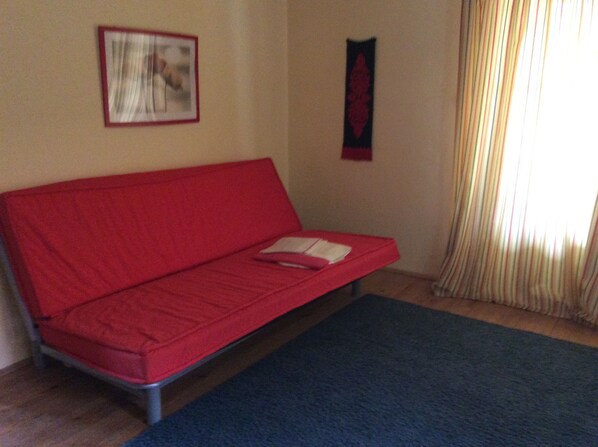 Un canapé rouge, un tapis bleu, une pièce avec une fenêtre et des rideaux.