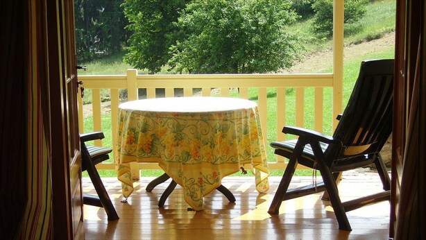 A wooden deck with a round table and two chairs, a white railing, and a view of greenery. - Spacious villa with fireplace (Vidochov)