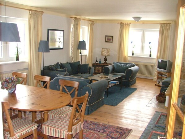 A living room with a sofa set, a dining table with chairs, a TV, and a lamp.