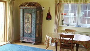 A room with a wooden cabinet, a table with chairs, a blue rug, and a window with curtains. - Spacious villa with fireplace (Vidochov)