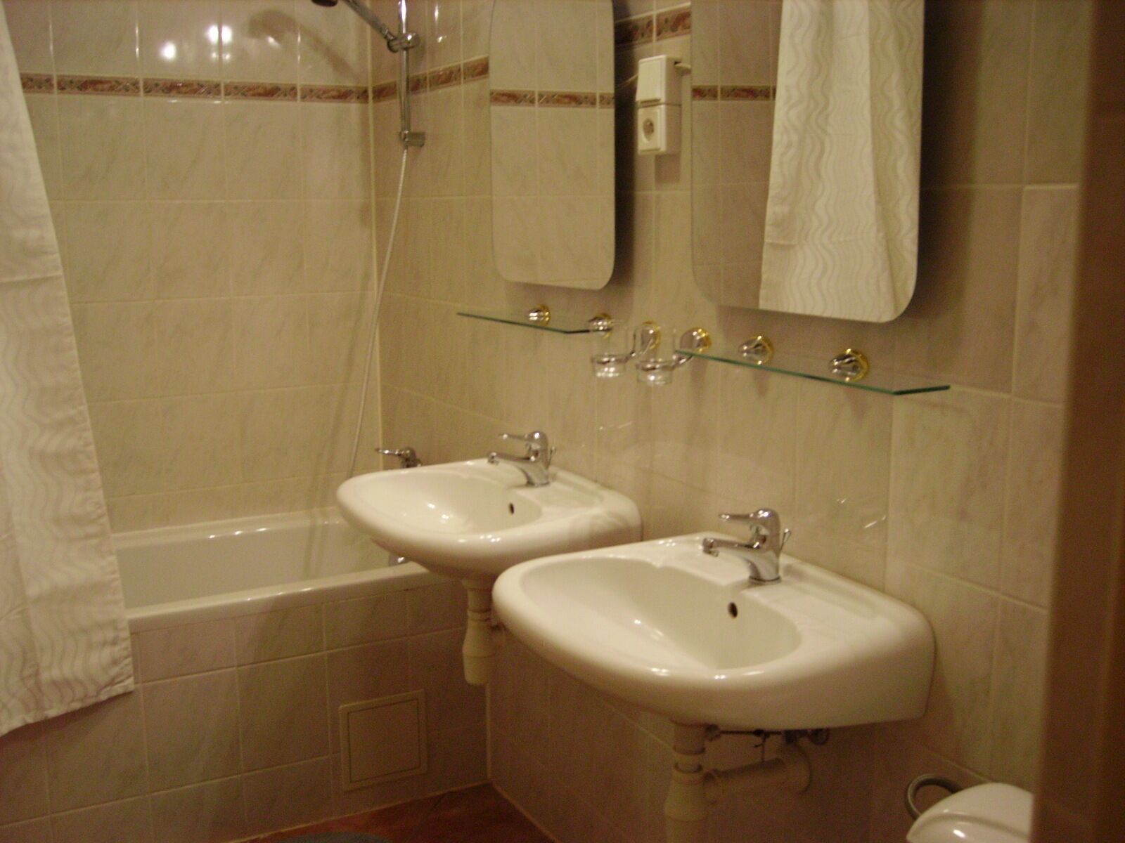 Een badkamer met twee wastafels, een bad en een glazen plank met toiletartikelen.