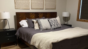 Ein Schlafzimmer mit einem Bett, zwei Nachttischen, einer Kommode, einem gemusterten Teppich und drei Wanddekorationen.