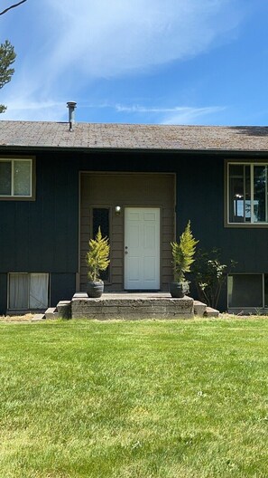 A two-story house with a dark exterior, a white front door, and a small porch with two potted plants.