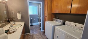A laundry area with a washing machine and dryer, a sink with a mirror, and a door leading to a bathroom. - Mountain View...walk to attractions & dining (Yelm)
