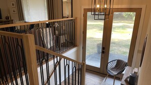 Ein modernes Interieur mit einer Holztreppe, einer Glastür, die auf einen Balkon führt, und einer Sitzecke mit Stuhl und Tisch.