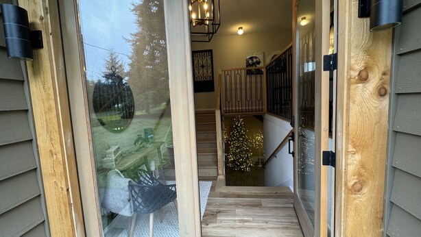 Eine Holztreppe führt zu einer zweiten Etage mit einer Glastür und Blick auf einen festlich geschmückten Weihnachtsbaum draußen.