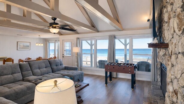 A spacious living room with a sectional sofa, a foosball table, and a large window offering a view of the beach. - Ocean's Edge | Pet-Friendly Oceanfront Home with Direct Beach Access (Ponte Vedra)