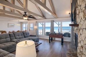 A spacious living room with a sectional sofa, a foosball table, and a large window offering a view of the beach. - Ocean's Edge | Pet-Friendly Oceanfront Home with Direct Beach Access (Ponte Vedra Beach)