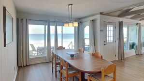 A spacious dining area with a wooden table and chairs, large windows with ocean views, and a ceiling with exposed beams. - Ocean's Edge | Pet-Friendly Oceanfront Home with Direct Beach Access (Ponte Vedra)