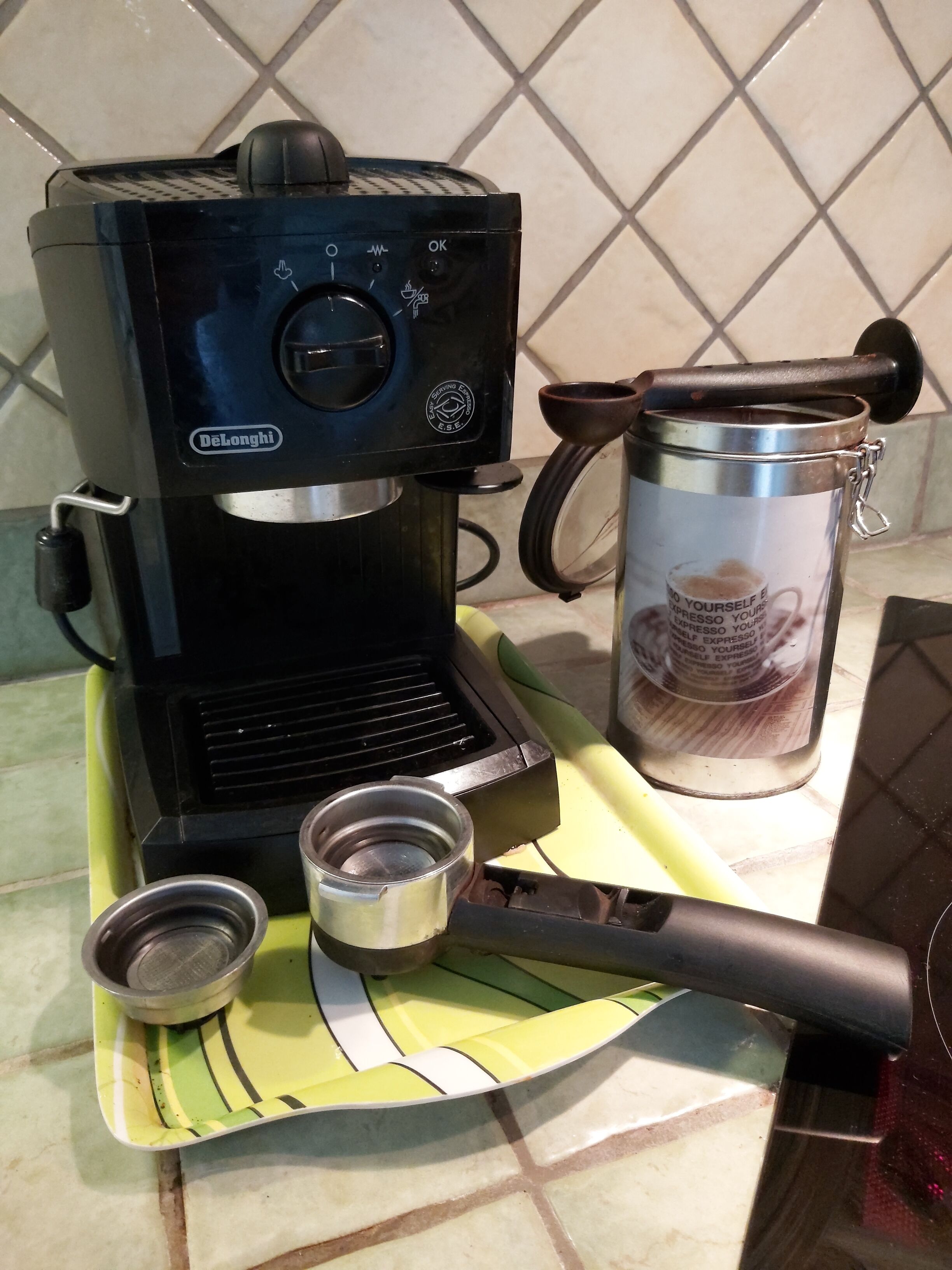 Una cafetera, un recipiente metálico y una cuchara sobre una encimera de cocina.