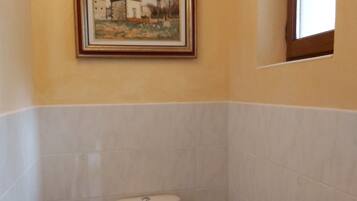 Een badkamer met een toilet, een inlijsting schilderij aan de muur, en een raam.
