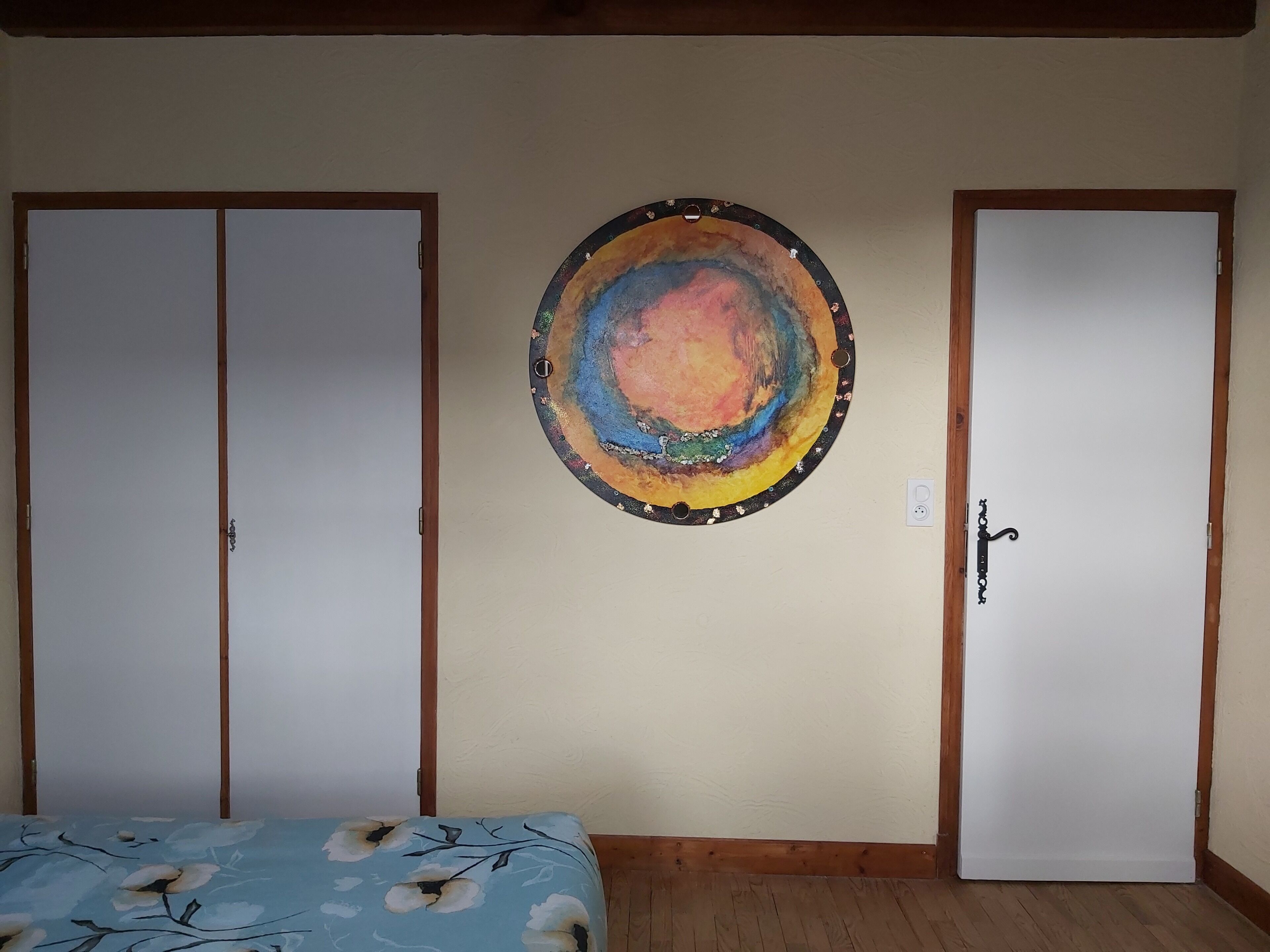 A room with two wardrobes, a bed with a floral bedspread, and a circular artwork on the wall.